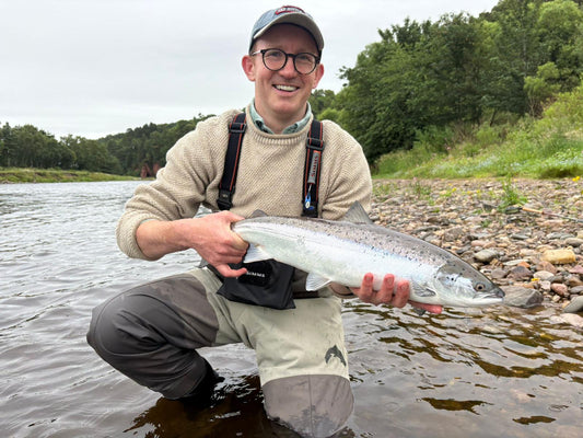 A salmon held for release in the river, the angler in waders and a cream fisherman's jumper.