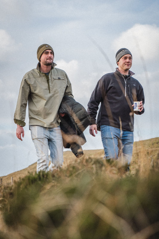 Hill Loch Shirt in Heather Green with a Kinloch Recycled Fleece Shirt in Charcoal, worn walking up through the hill grass.