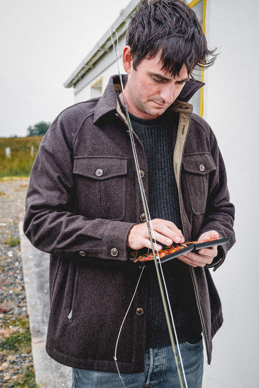 Arkle Wool Jacket, worn over a navy knit while choosing a fly from an open fly box, rod in hand.