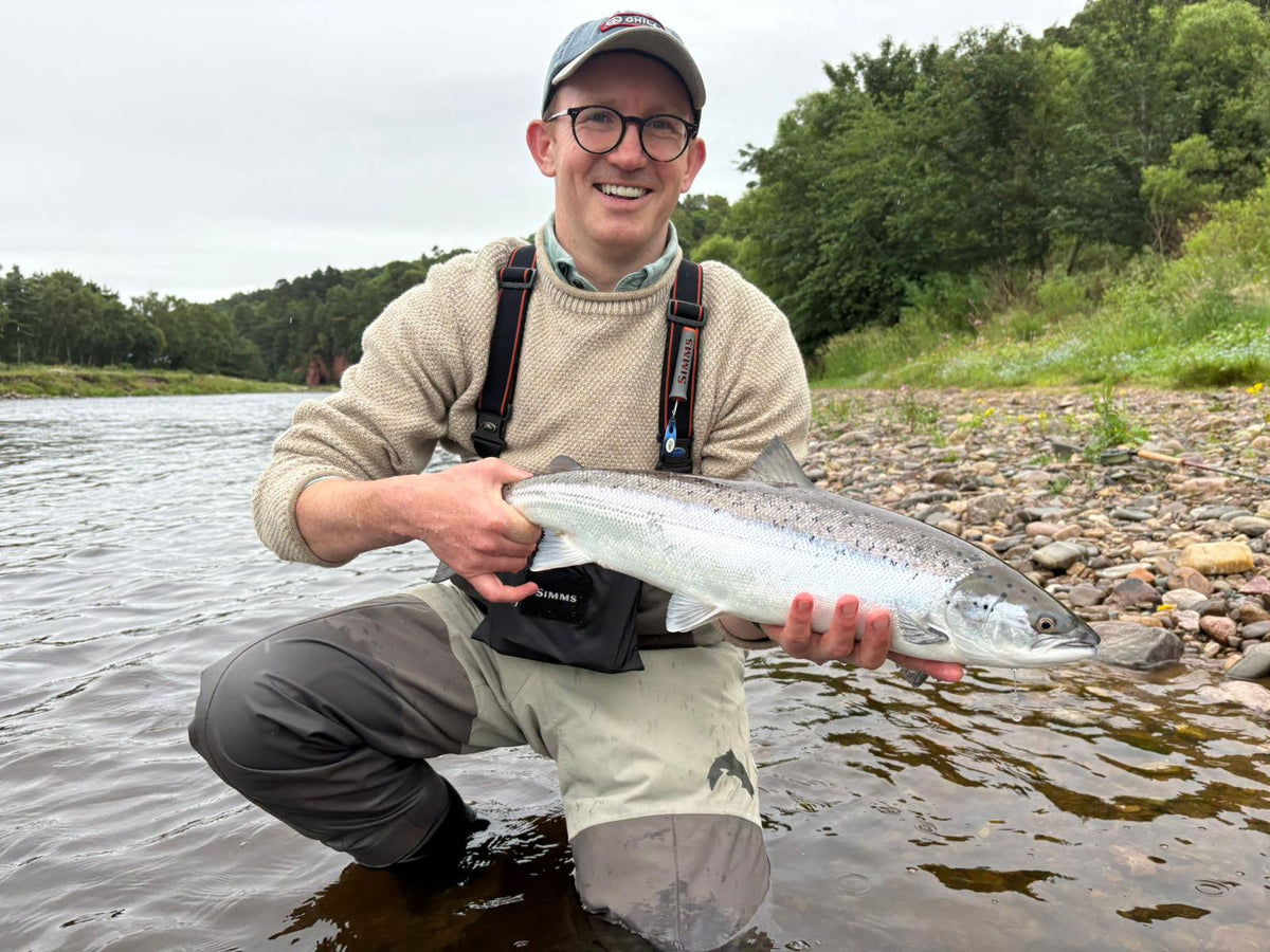 A salmon held for release in the river, the angler in waders and a cream fisherman's jumper.