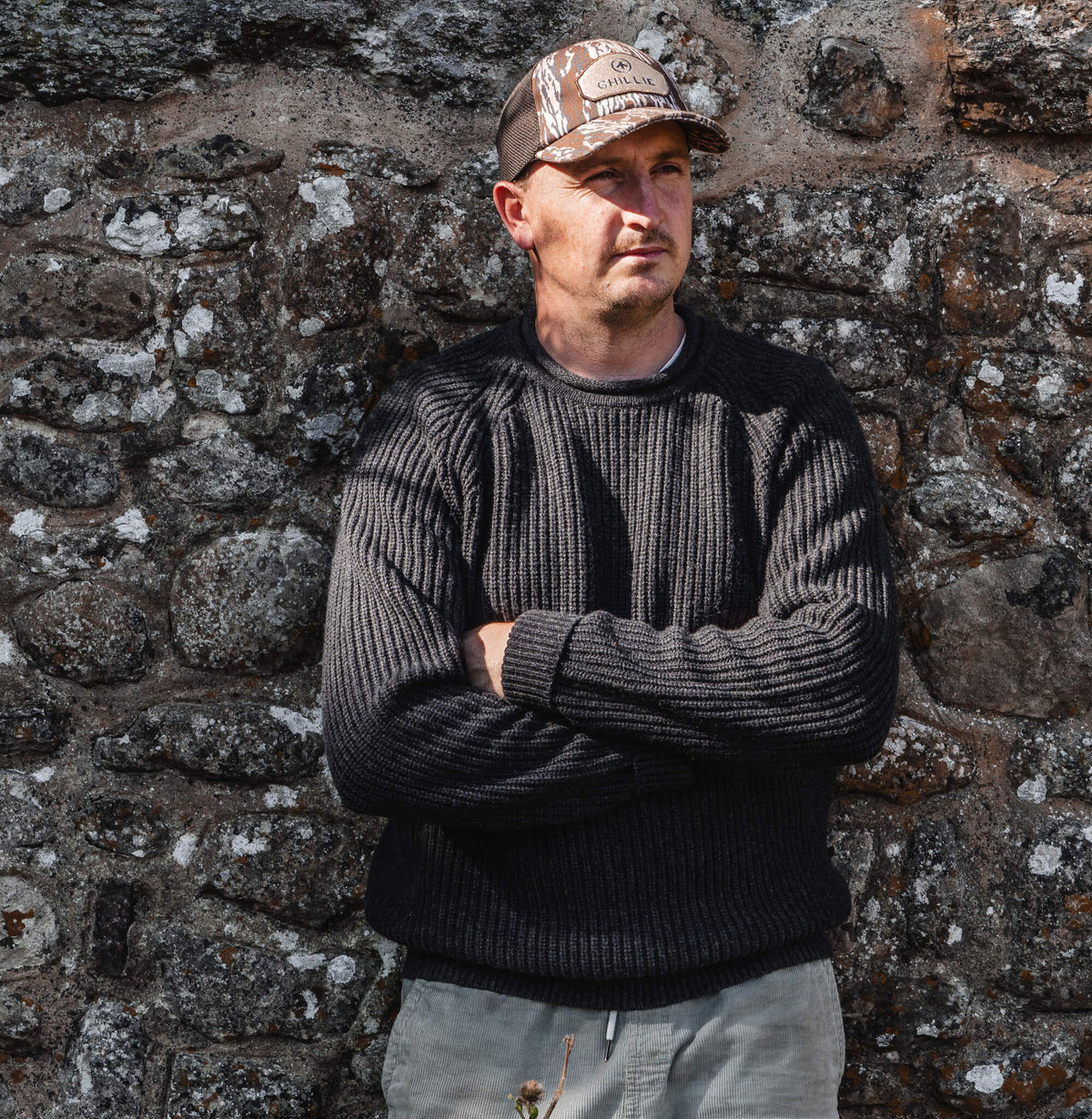 Tarbert Fisherman's Jumper in Slate, worn against a drystone wall.