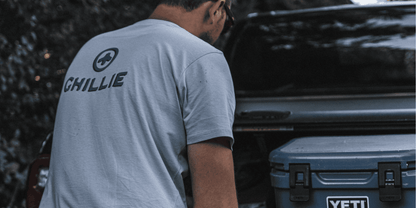 Logo Tee in Sea Fog, worn at the tailgate beside a cool box.