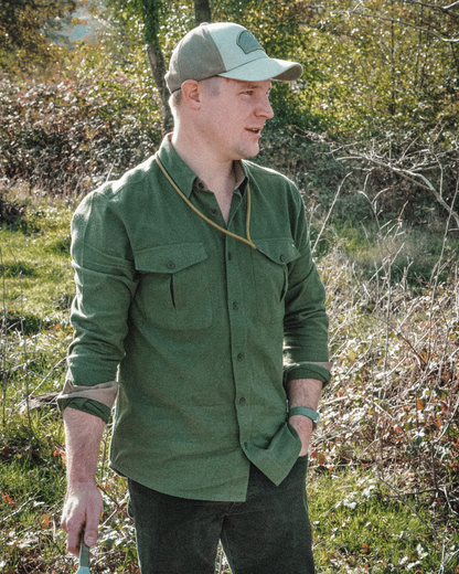 Munro Flannel Shirt in Rifle Green with an Original Trucker Cap in Lichen Green, worn with sleeves rolled at a sunlit woodland edge.