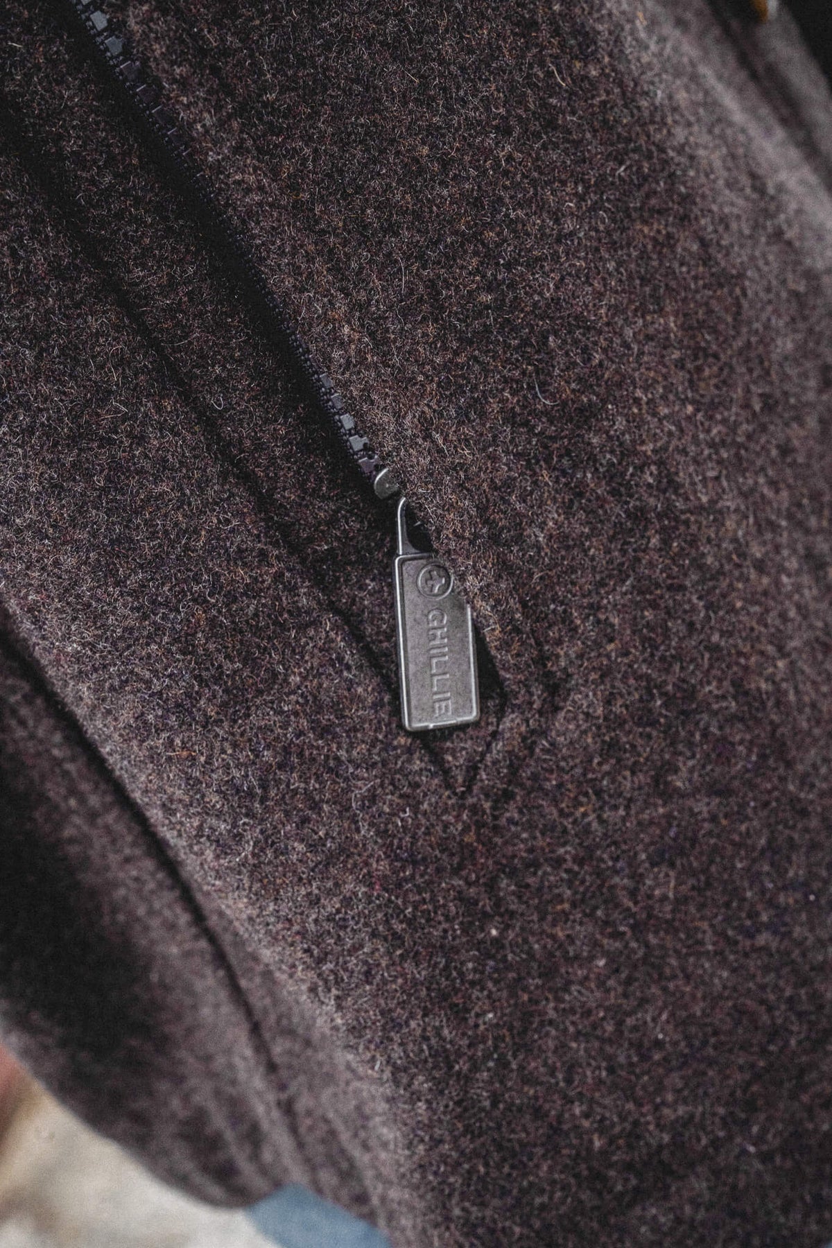 Arkle Wool Jacket, close view of the dark brown wool and the metal pocket zip pull stamped with the Ghillie name.